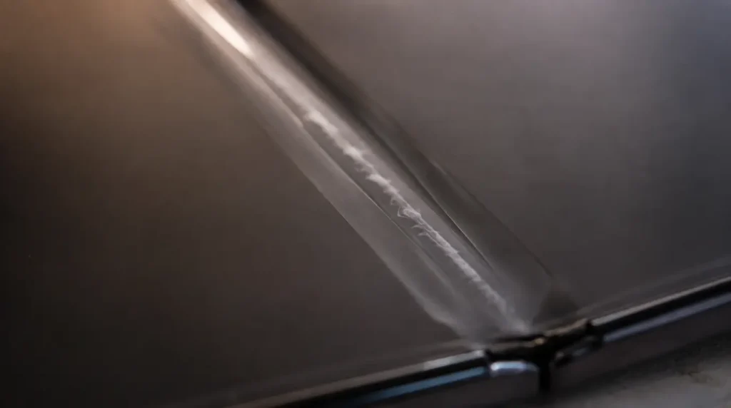 Macro shot of foldable phone crease showing stress line under bubbled screen protector on display panel